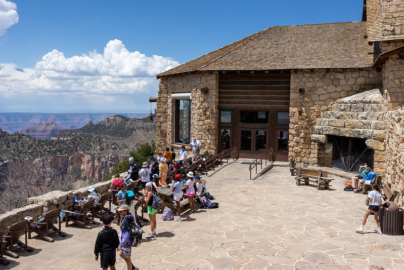 A group of 20 people gather on the outdoor veranda outside the North Rim Lodge with a canyon landscape in the background.