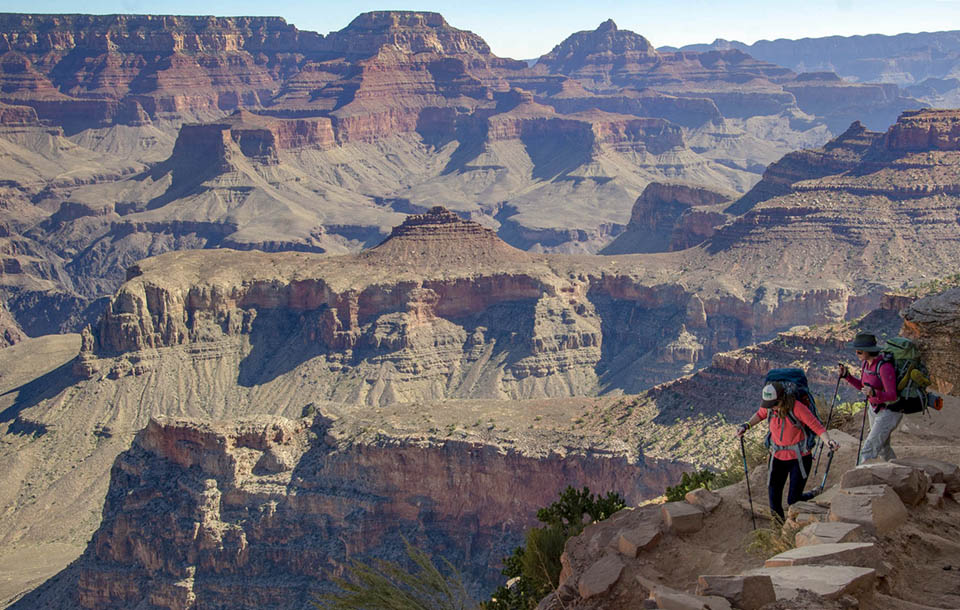 Two hikers descend down a hot, steep trail into the colorful cliffs of Grand Canyon.