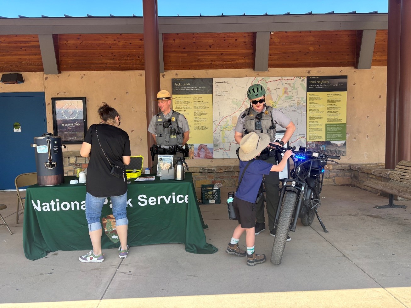 Two uniformed rangers in law enforcement gear talk to visitors next to a green table.