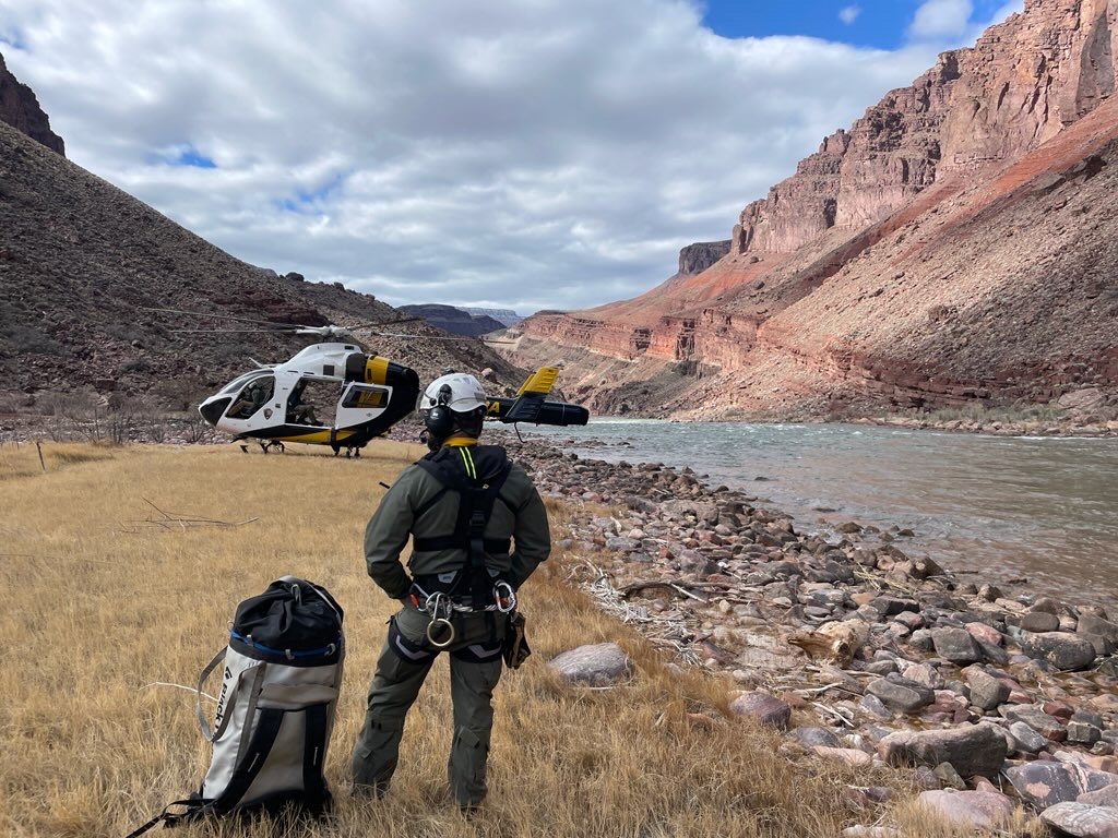 A helicopter and responder are next to a river in a canyon