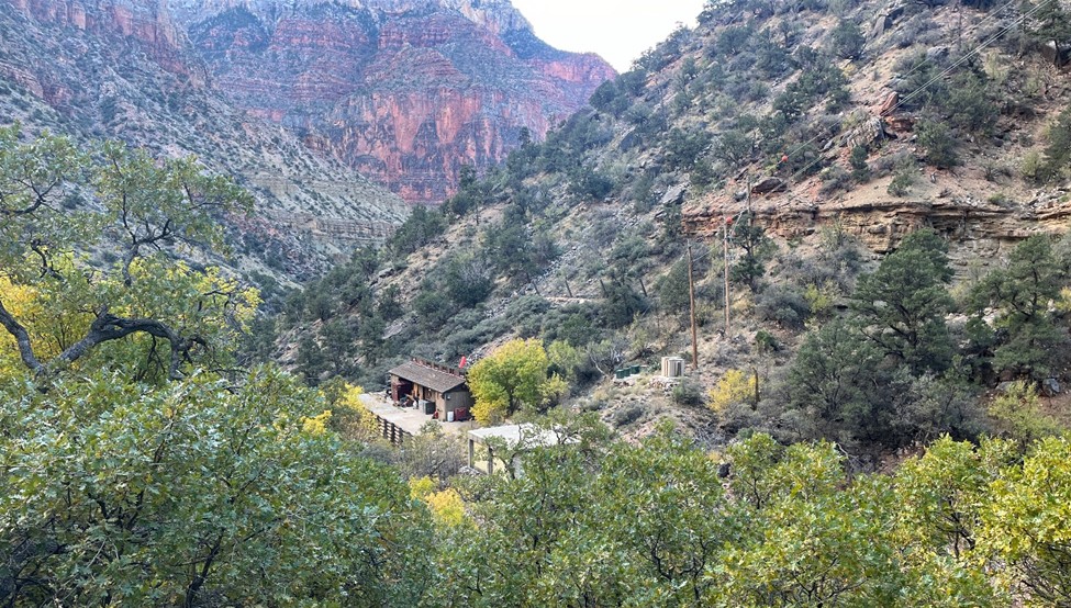 A small brown house in the middle of a canyon with trees surrounding