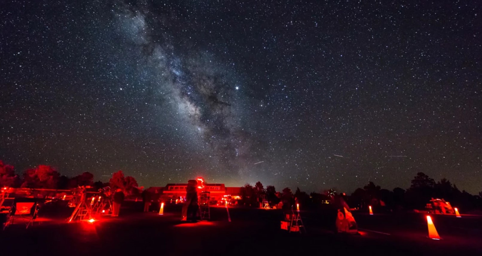 Telescopes are propped under a starry night sky with the milky way shown