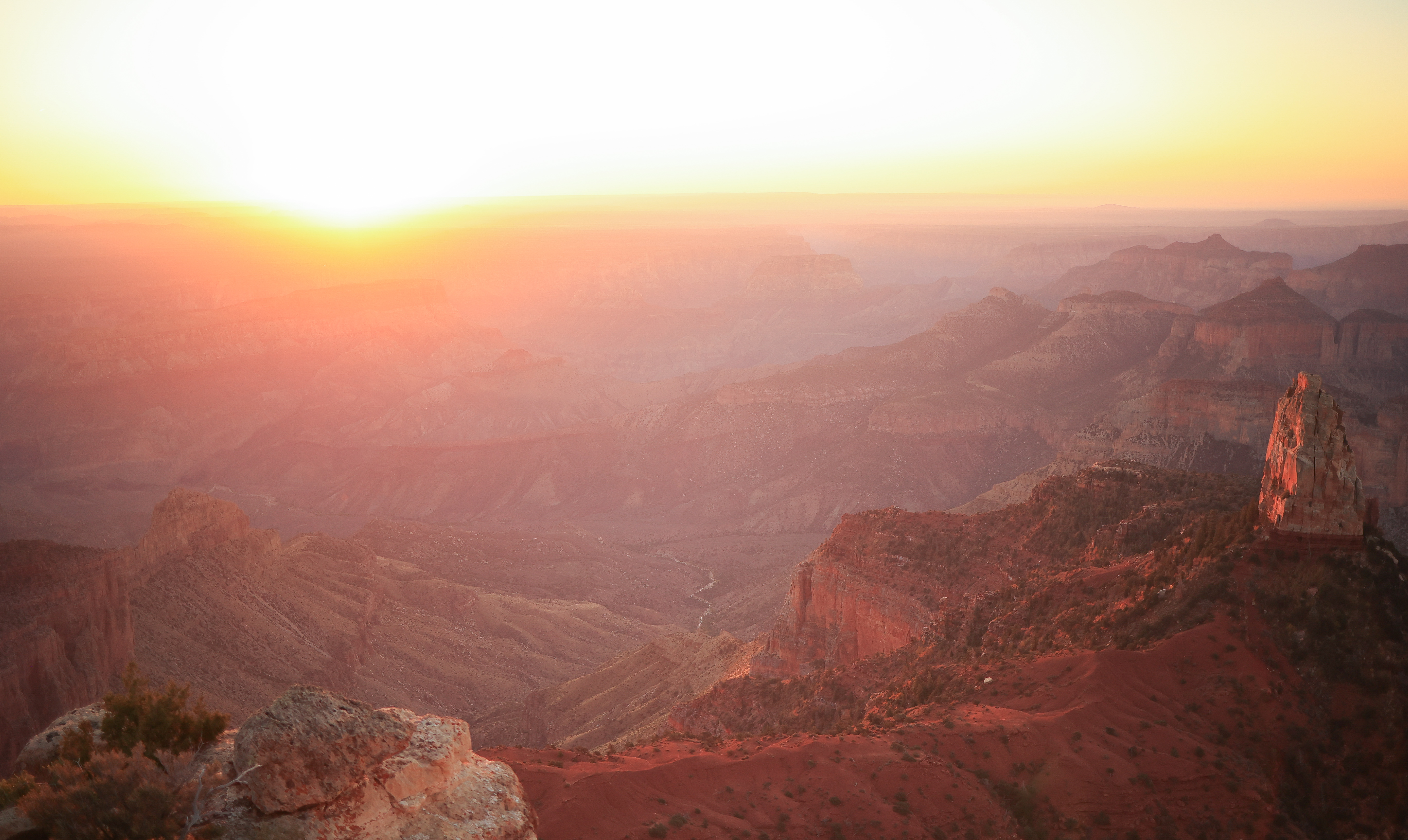 A warm sunrise of pink and orange over a canyon landscape