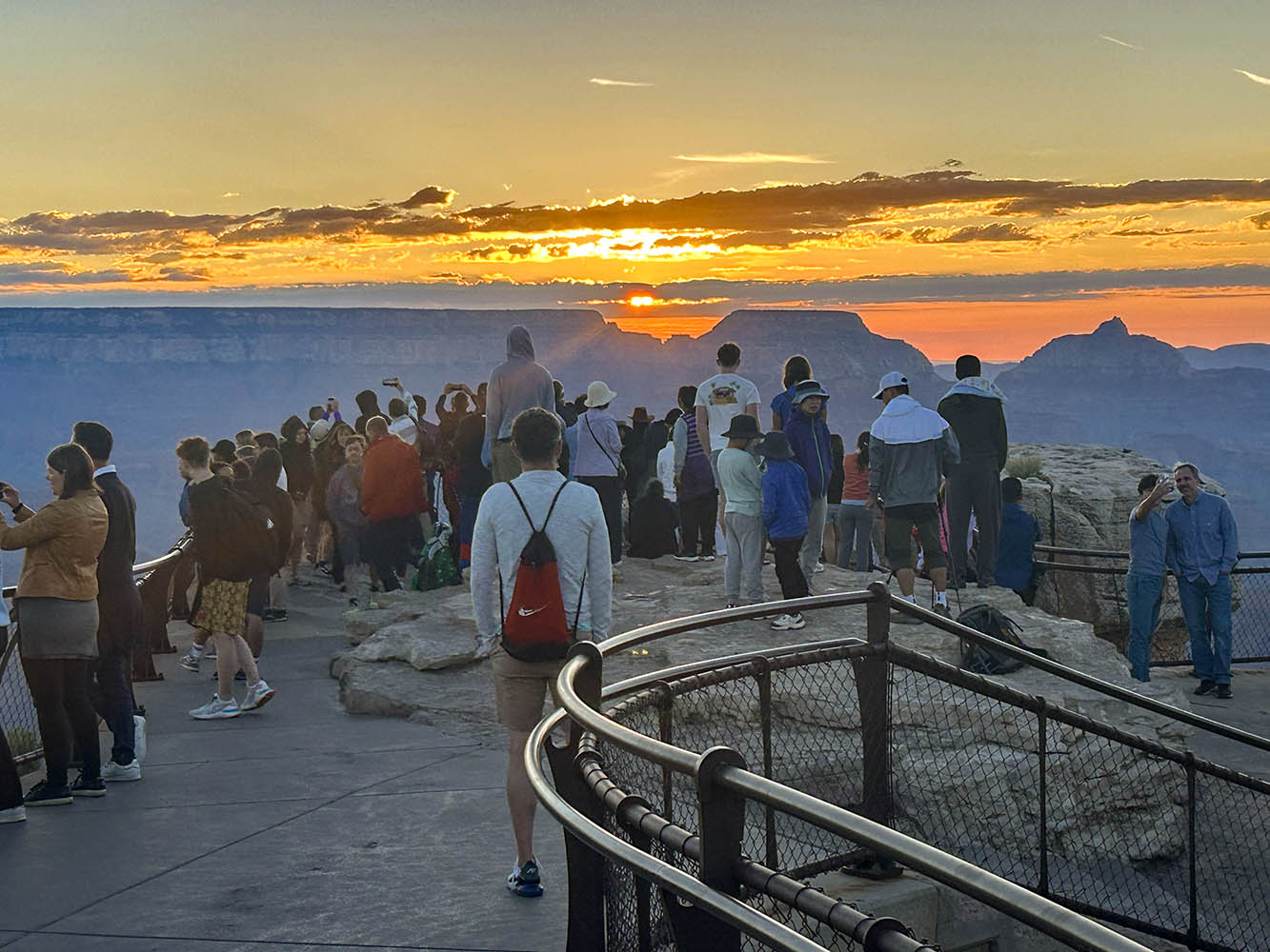A crowd of 20 people gather at Mather Point and take in the brilliant yellow and pink sunrise from the rim of the canyon