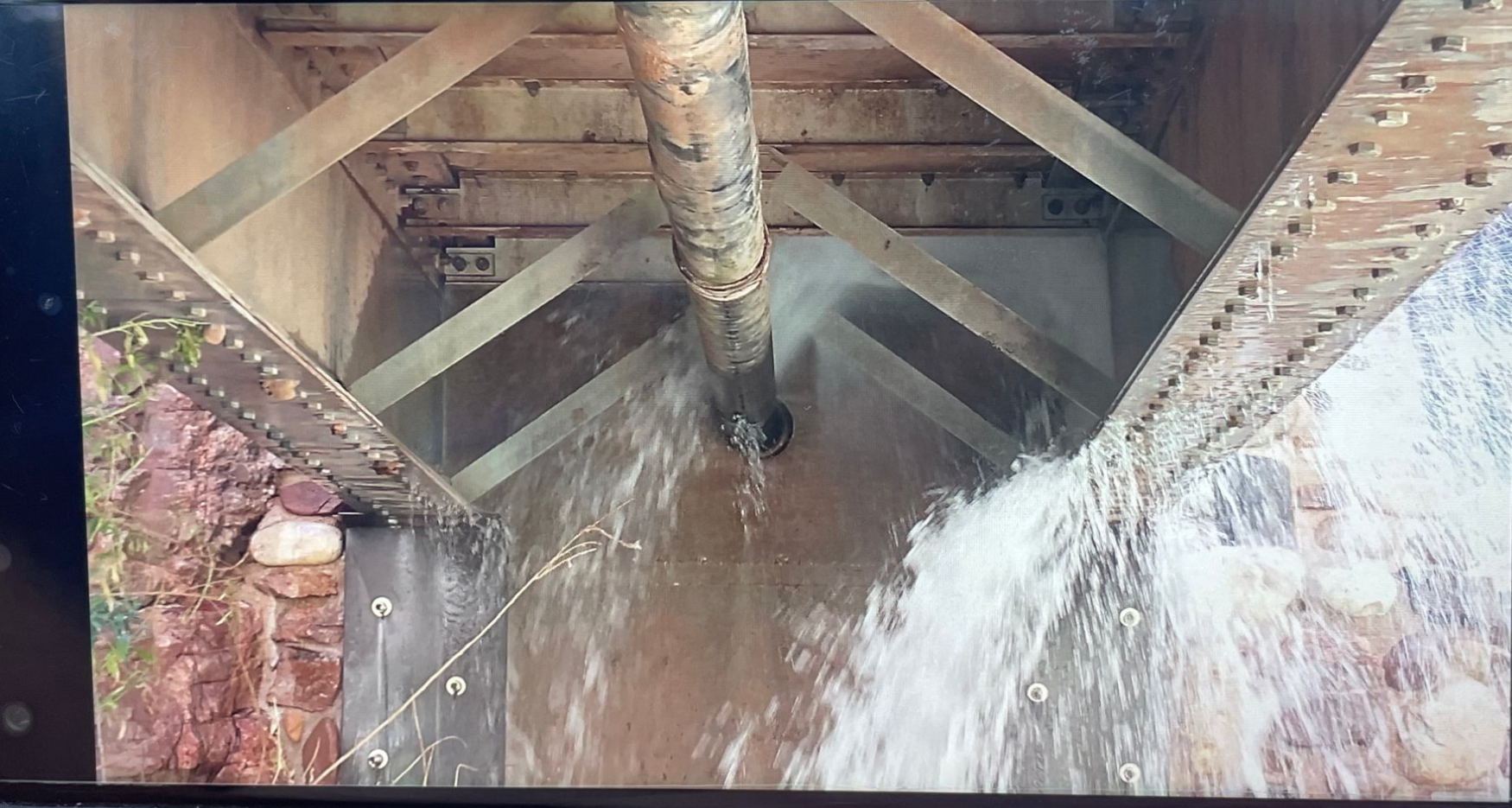 A pipe underneath a bridge gushing with water