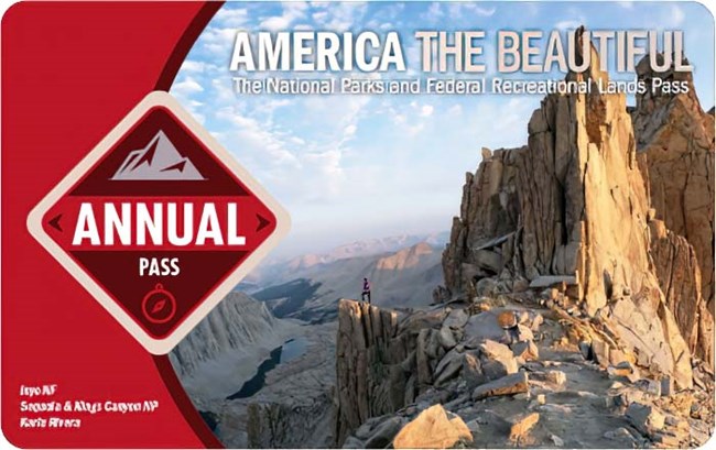America the Beautiful 2023 Annual pass shows a backcountry trail ending at an overlook atop a jagged mountain peak, the words "annual pass" is displayed within a red diamond on the left.