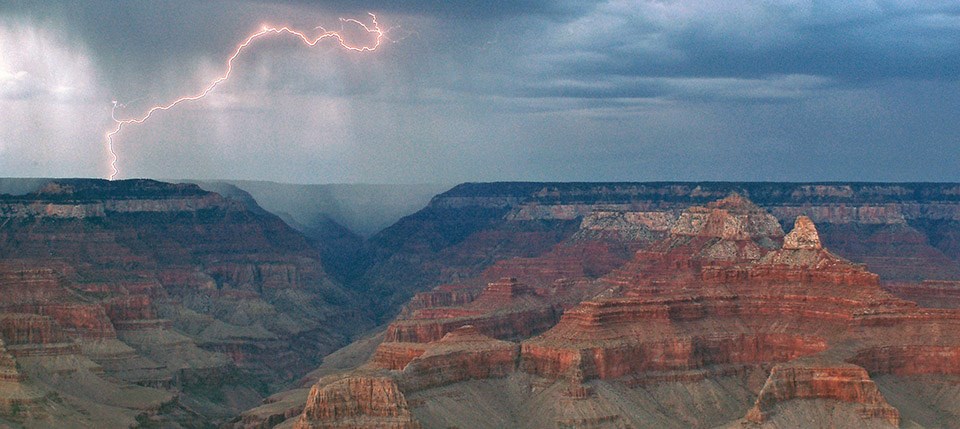 Looking out across the canyon during a storm. A bolt of lightning on the far left hitting the canyon rim on the north side.