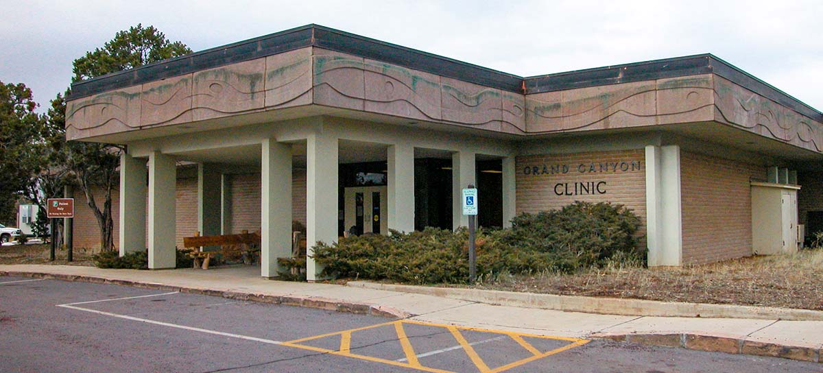 A modern boxy, beige brick colored building with an extended portico held up by cement pillars. A decorative frieze that could be waves or snakes, wraps around the building just below the roof.