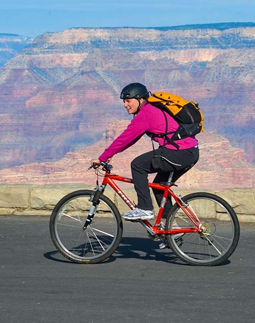 Smiling woman riding a red bicycle along a paved road with colorful canyon walls beyond.