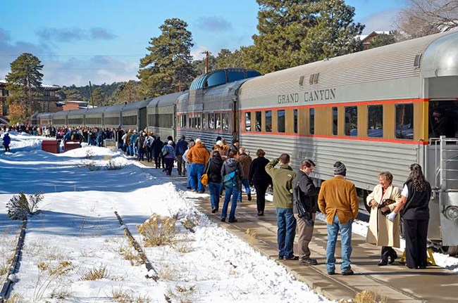 With snow covering the ground, seven vintage railroad passenger cars in a row as several hundred people are getting off the train.