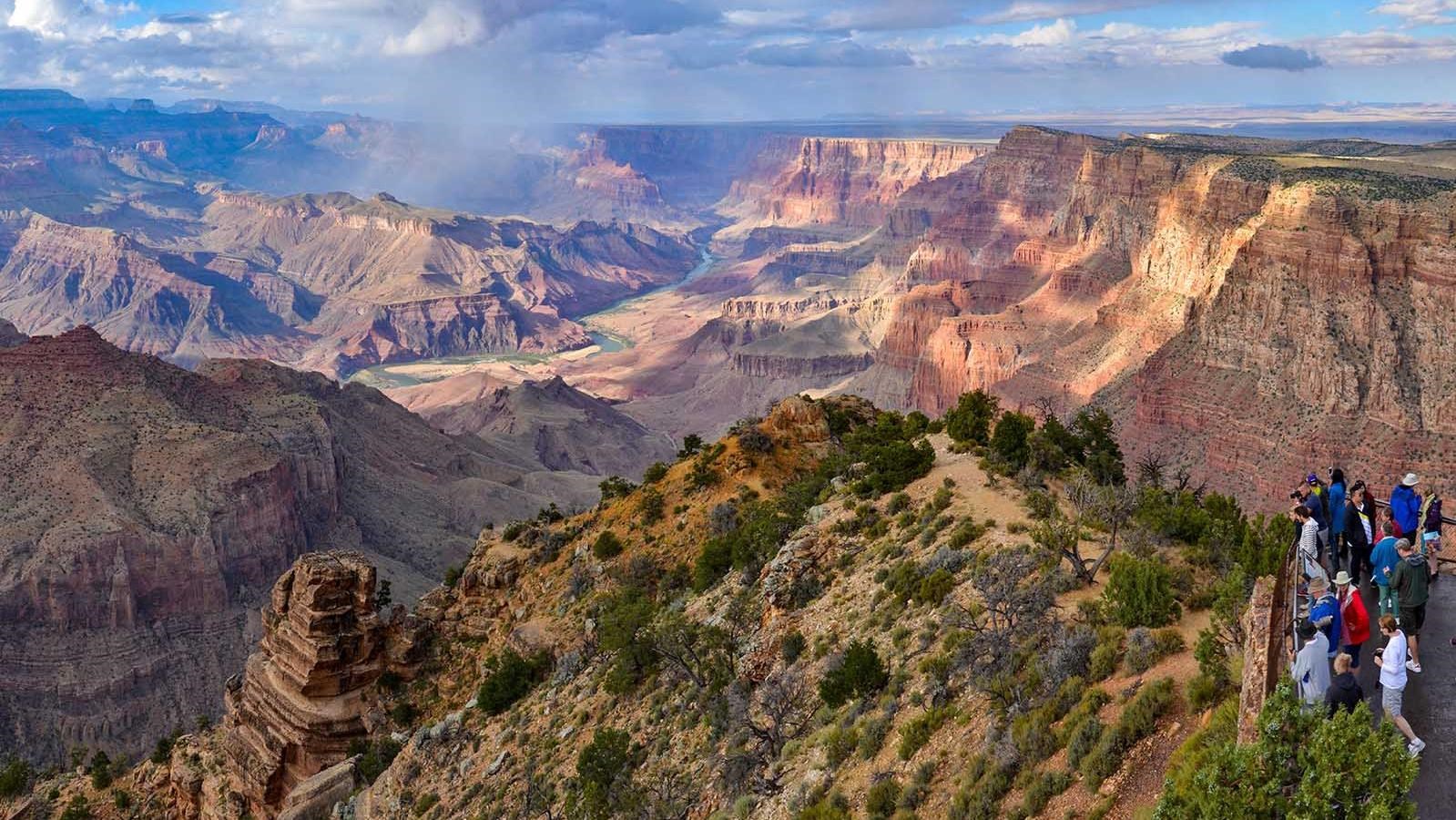 On the right, behind a guardrail at a scenic overlook, a dozen sightseers are viewing a river flowing within cliff walls a mile below,