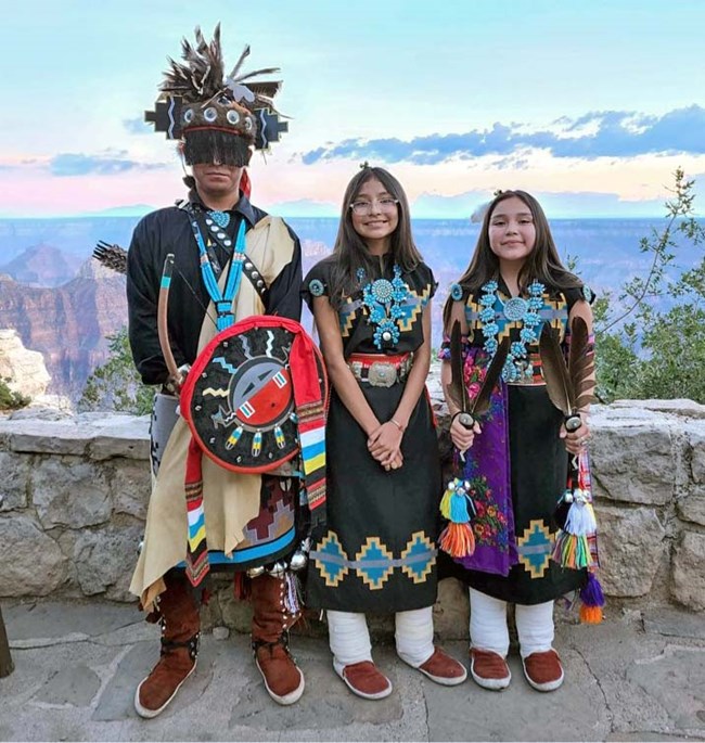Three young Navajo dancers are posing for a group photo in their traditional clothers.
