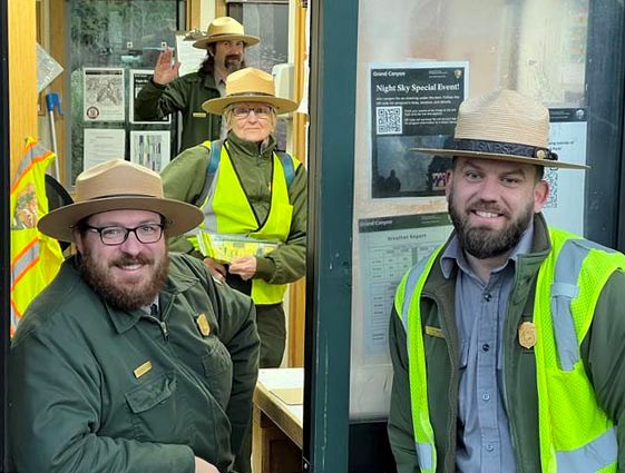 four fee collection park rangers pose for a photo in and just outside of a fee booth window.