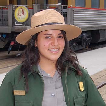 A female ranger in uniform standing in front of a passenger train car.
