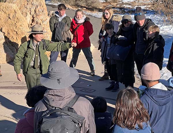 A park ranger is giving a program outdoors and interacting with visitors who are wearing winter clothes and hats.