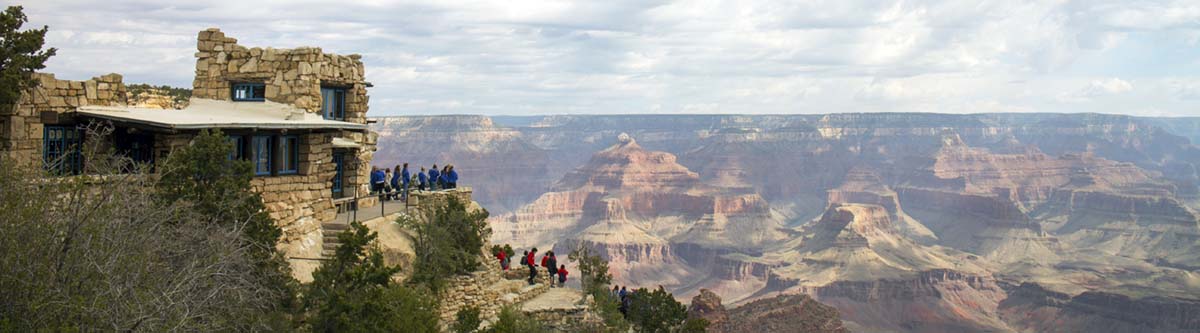 on the left, rustic stone observation building. to the right, a complex landscape of colorful pinnacles and peaks within Grand Canyon