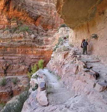 Two hikers descend a switchback and a series of steps along a steep canyon trail