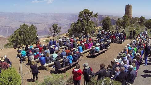 Around 100 people gathered for the rededication of Desert View Watchtower. The audience, seated on benches in the foreground are near the edge of Grand Canyon. the Watchtower is seen off in the distance.