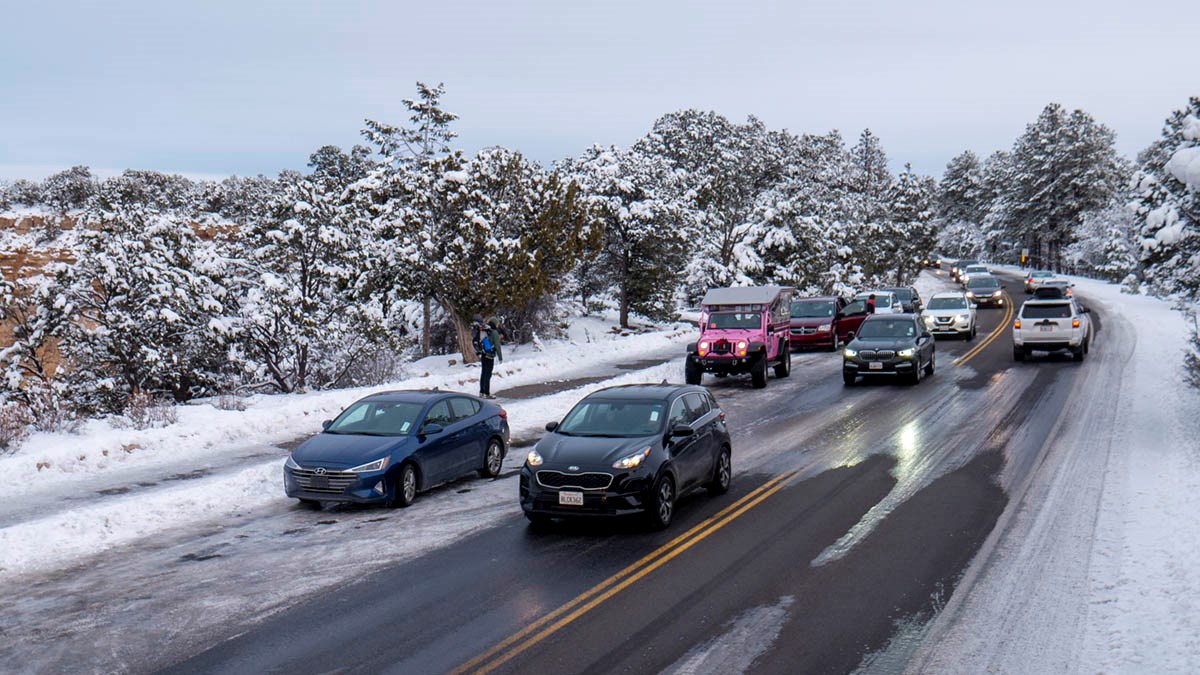 Ten cars driving over icy patches in a roadway by a pull-off at a scenic overlook