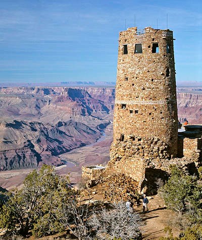 A cylindrical, 4-story, stone tower, 70 feet (21 m) tall, on the edge of a vast, mile-deep canyon with vertical cliff walls.