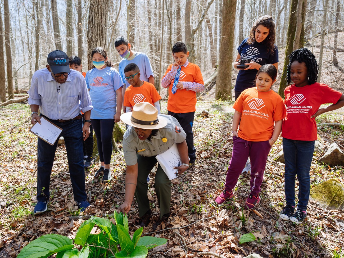 Ranger bends over to touch large leafed plant on ground while kids and chaperones watch.