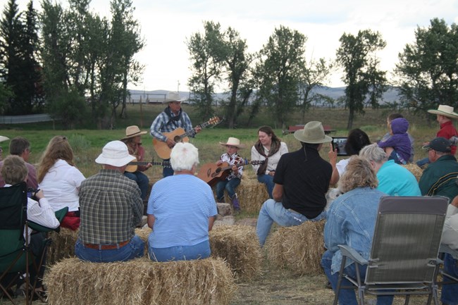 Visitors sit on hay bales around the campfire as cowboy singers perform.