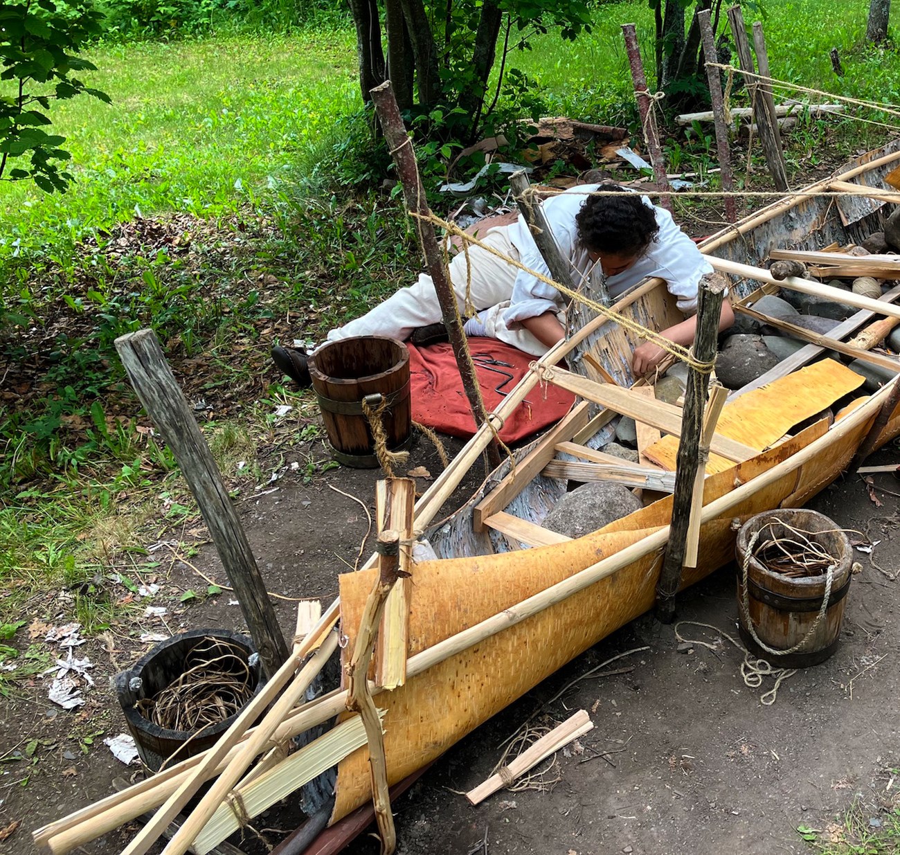 A reenactor sews additional bark to the sides of the canoe.