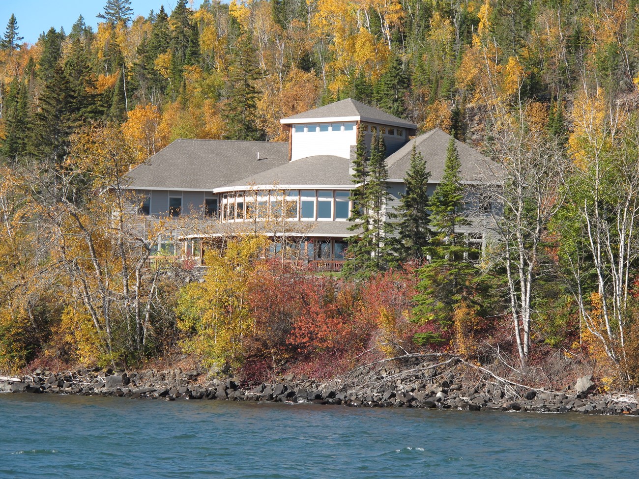 A building with many windows on a hill, nestled among fall colored trees.