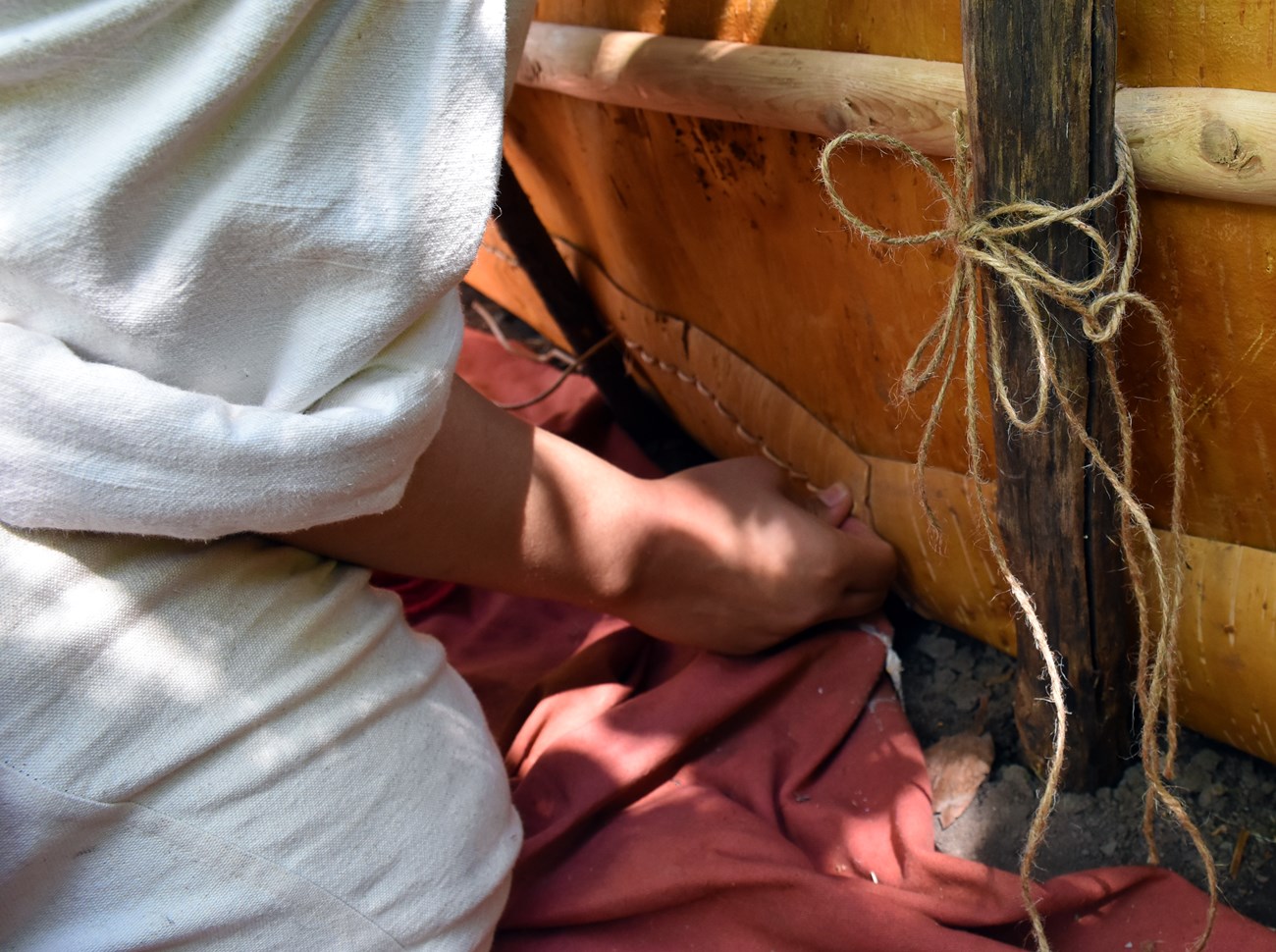 Detail of hands with spruce root along a bark canoe side.