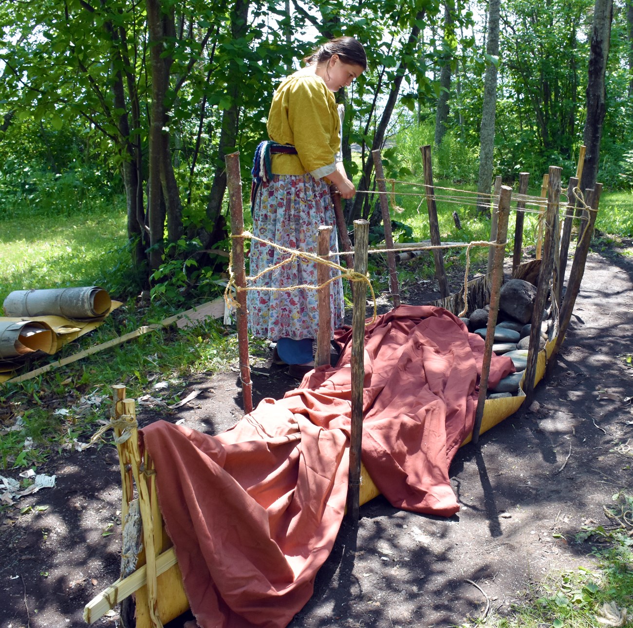 A reenactor places stakes to form the sides of a canoe.