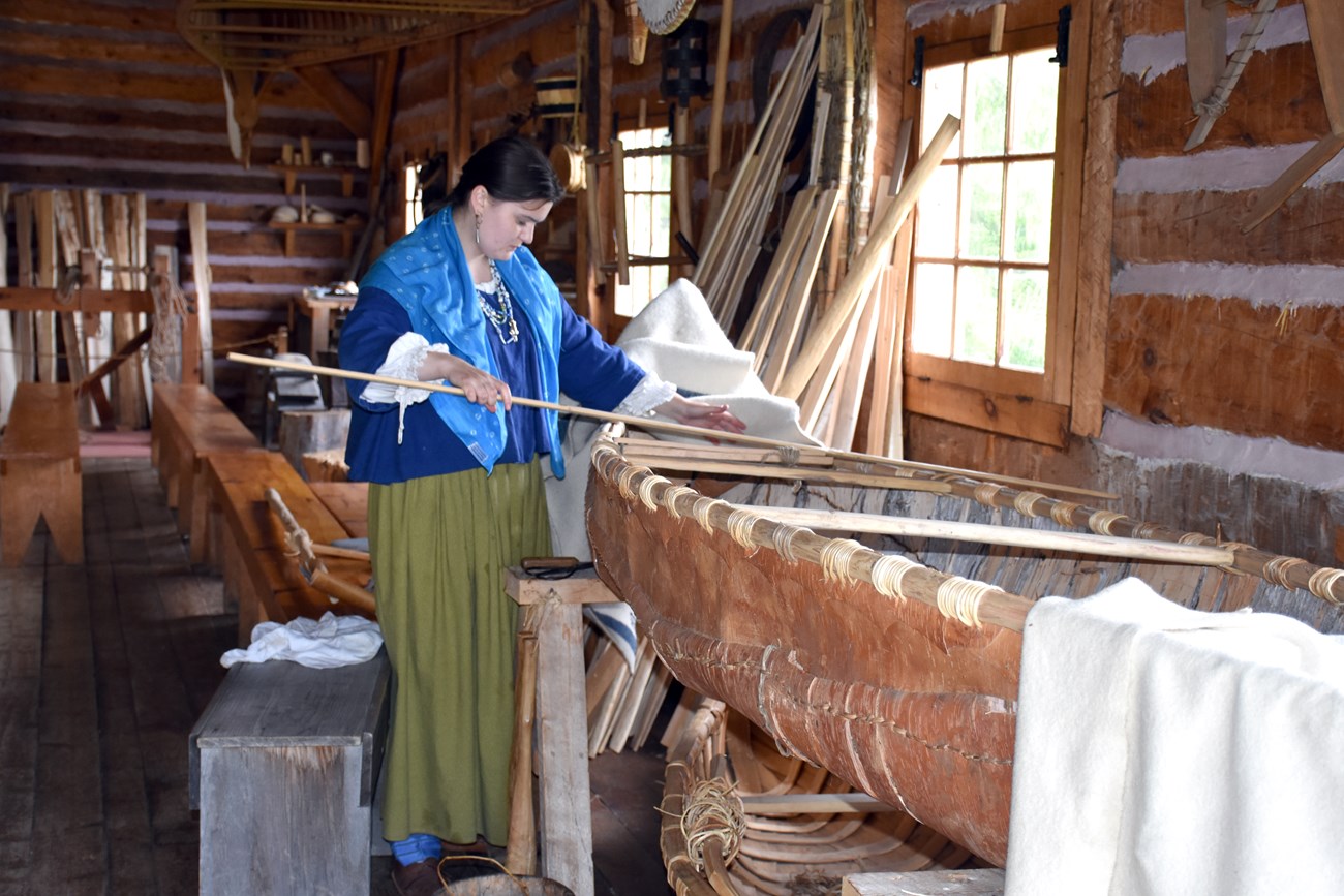 A person in historic clothing measuring a canoe thwart.