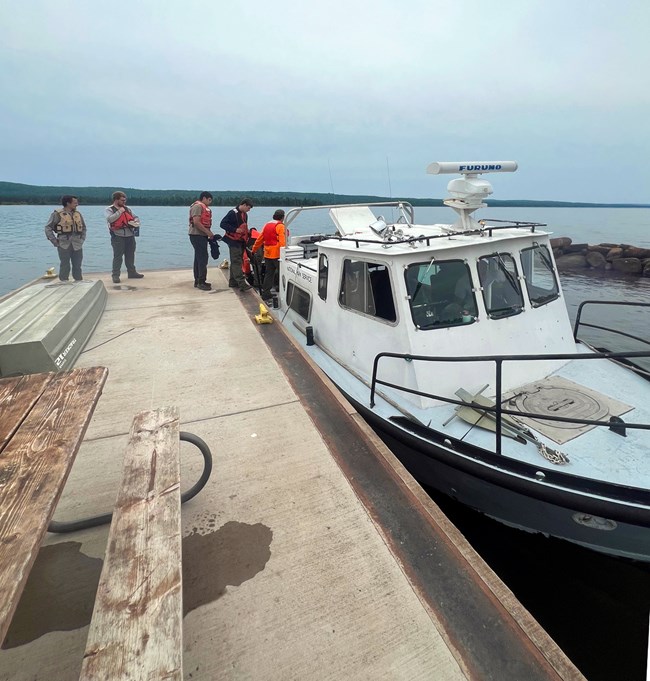 People standing on a dock next to a boat on a lake.