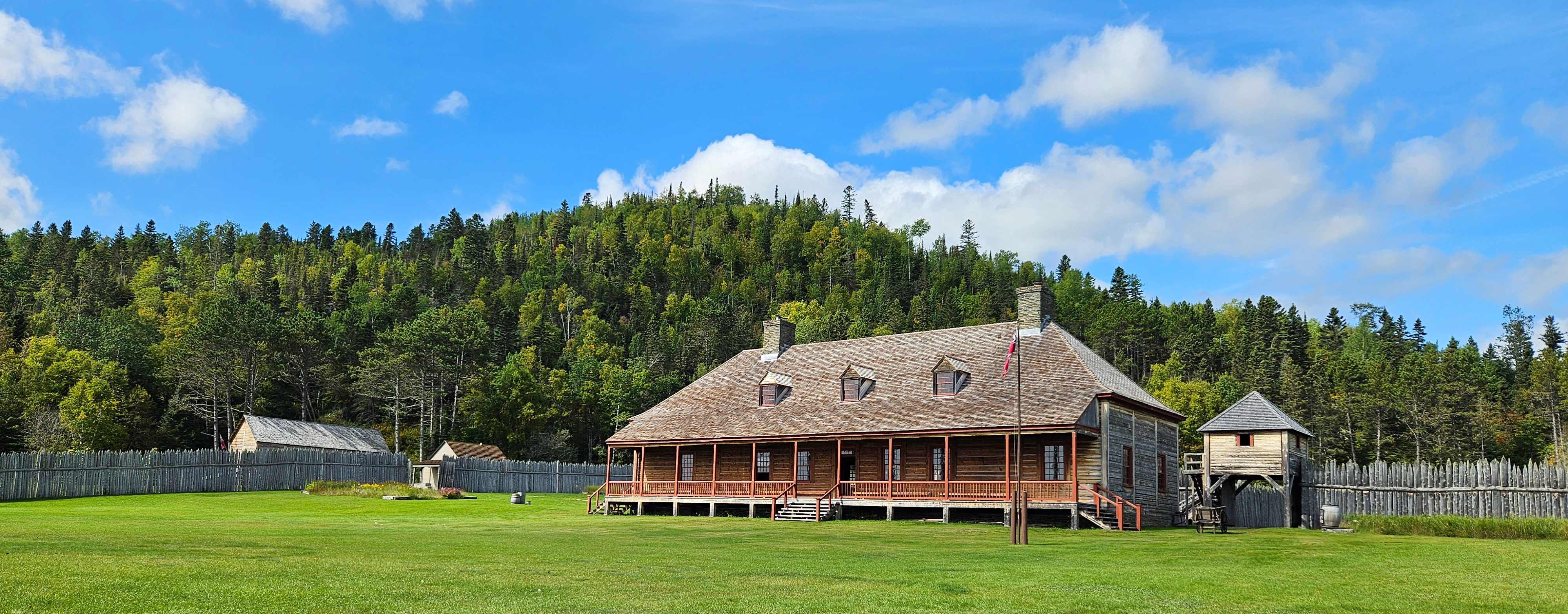 Historic wooden buildings in front of a tree-covered hill.