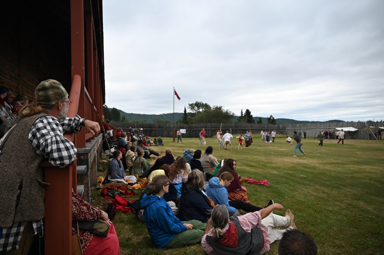 A crowd sitting on the Great Hall lawn watching a lacrosse game