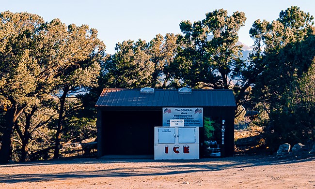 A small wooden store is situated in pinyon pine trees with an ice machine at front.