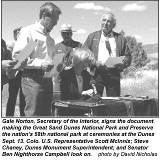 Several people stand around a table as the Secretary signs a document.