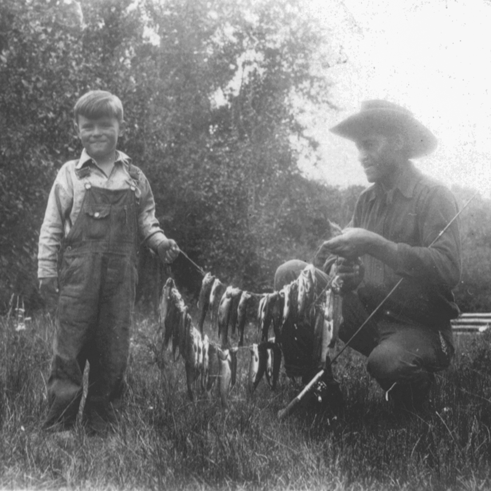 In this historic photo from the early 20th century, Black cowboy Frank Jackson holds a large string of trout with his young friend Jack Williams.
