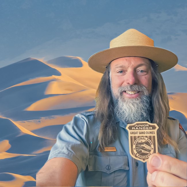A park ranger in flat hat holding a wood junior ranger badge