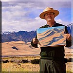 Park ranger holding a color sketch of the dunes, with the dunes and snowcapped mountain in the background