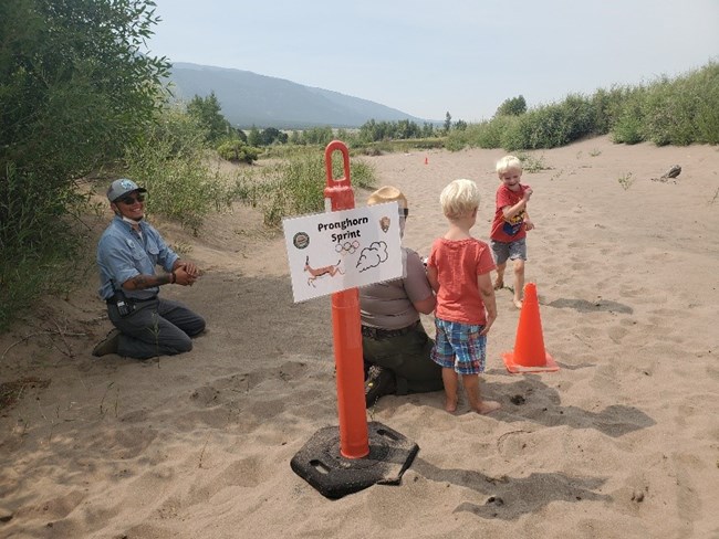 A ranger and intern help two children do an activity on the sand at Junior Ranger Day
