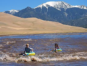 Two children floating Medano Creek with dunes and mountain behind