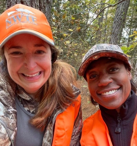 Two women smile wearing hunter orange and camouflage