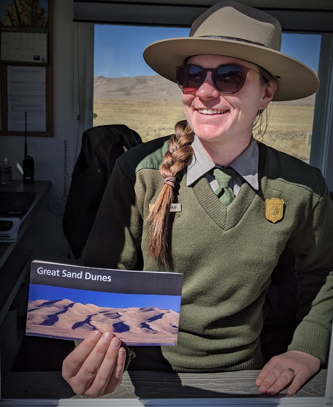 A park ranger inside the park's entrance station greets visitors to Great Sand Dunes with a park map.