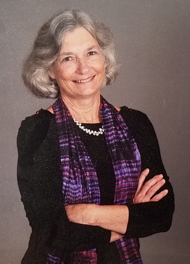 Nancy Arbuthnot standing with arms folded in a black dress and purple shawl