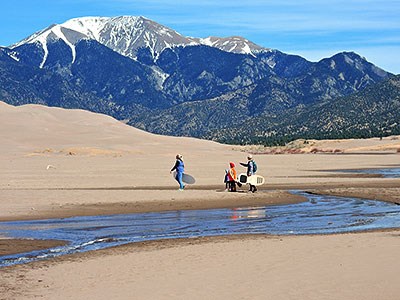 Medano Creek at low flow, visitors hiking, dunes, and snowcapped mountain
