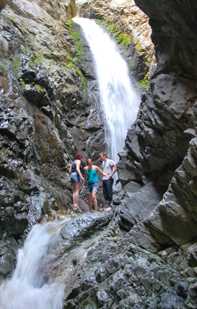 People stand below a waterfall in a crevasse