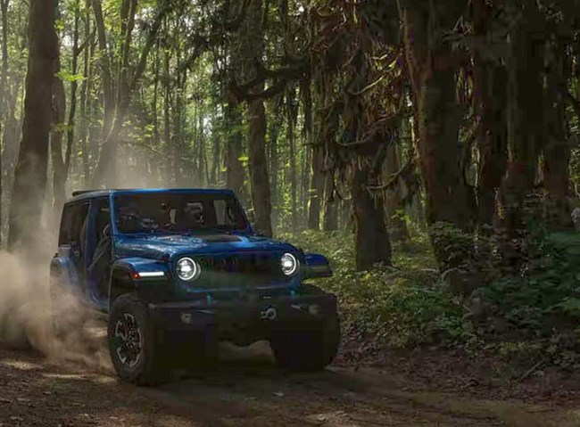 A blue Jeep drives on a forested road