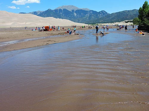 A shallow stream flowing at the base of dunes and a mountain