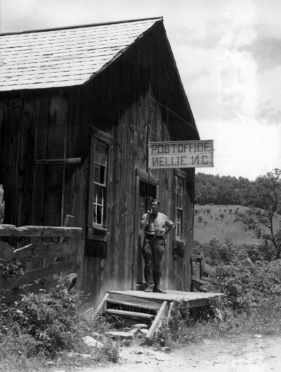 Man standing on the front porch of the Nellie Post Office in Cataloochee.