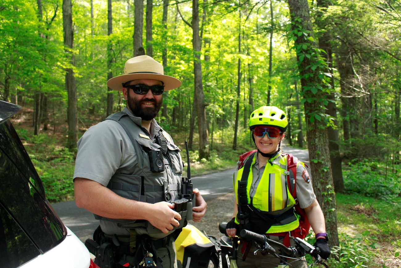 One law enforcement ranger and one ranger in bright yellow high visibility gear stadning for a photo along a road in the forest